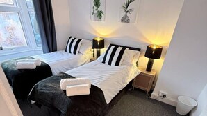 Ein Hotelzimmer mit zwei Betten, einem Fenster mit Vorhängen, einem Heizkörper und einer an der Wand befestigten Pflanze.