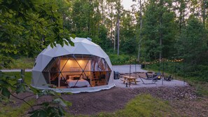 Eine geodätische Kuppel mit einem Bett, einer Sitzecke und einem Tisch in einer Waldlandschaft.