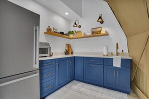 Eine Küche mit blauen Schränken, einem Edelstahlkühlschrank und einem Holzregal mit verschiedenen Gegenständen.