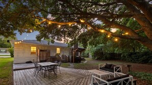 Eine Holzterrasse mit Gartenmöbeln, einer überdachten Veranda und Lichterketten.