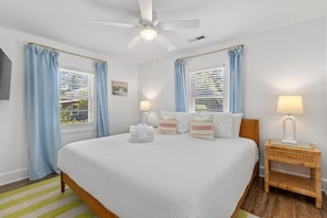 A hotel room with a bed, a ceiling fan, a nightstand, and a window with curtains.