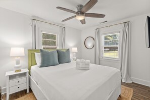 Une chambre à coucher avec un lit, des tables de chevet, un ventilateur de plafond et des fenêtres avec des rideaux.