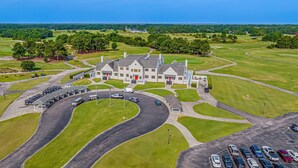 A golf course with a clubhouse, parking area, and surrounding greenery. - On the Links-9th Hole- L egends Stay (Myrtle Beach)