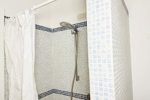 Une douche équipée d’un pommeau de douche à main, d’un rideau blanc et de murs carrelés avec une bordure bleue.