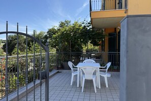 Un balcon avec une table et des chaises, entouré d’une clôture en métal et agrémenté de plantes en pot.