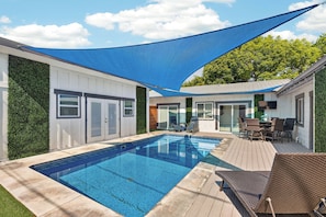 Ein Pool mit einer Liegefläche, Sitzgelegenheiten im Freien und einem schattigen Bereich.