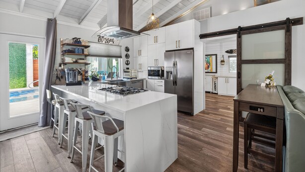 A modern kitchen with a central island, bar stools, stainless steel appliances, and a large window. - Completely re-done 4 bedroom pet-friendly home. Great location. (St. Simons Island)