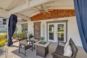 Eine überdachte Terrasse mit Deckenventilator, einer Willkommensschild und Gartenmöbeln.