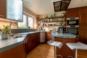 Eine moderne Küche mit Holzausstattung, einem Edelstahl-Spülbecken, einem eingebauten Ofen und einer Bar mit Hockern.
