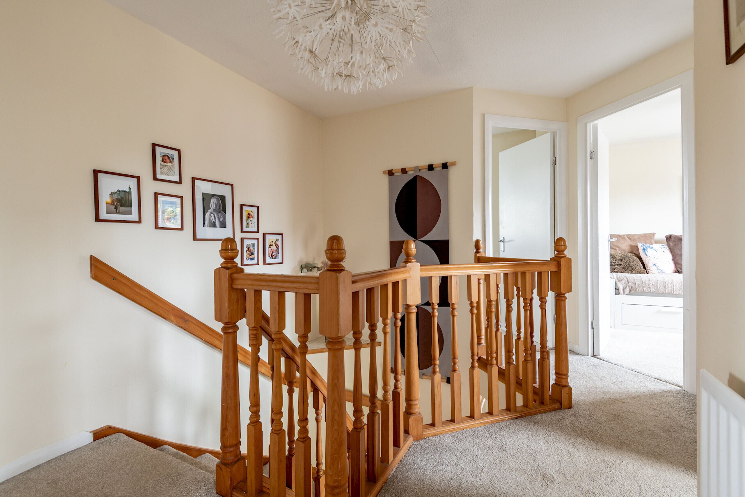 A staircase with wooden railings, a chandelier, and framed pictures on the wall.