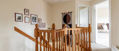 A staircase with wooden railings, a chandelier, and framed pictures on the wall.