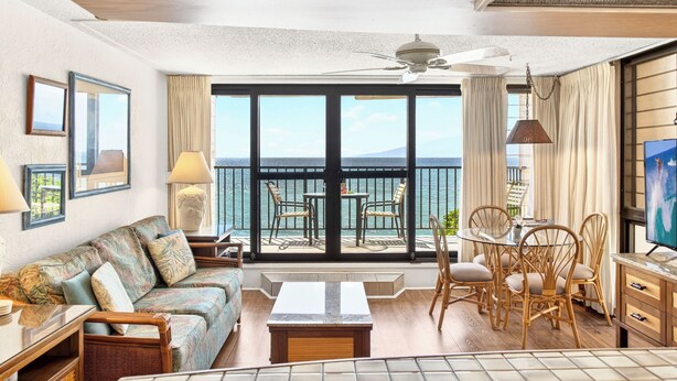 Una habitación con sofá, mesa de comedor, sillas, televisor y un balcón con vistas.