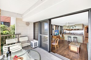 Ein Balkon mit Glastür, der zu einer Küche mit Fernseher, Holzstühlen und einem Esstisch führt.