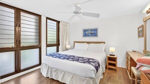 Un dormitorio con cama, mesita de noche, escritorio, silla y ventilador de techo.
