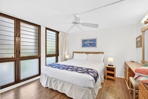 Ein Schlafzimmer mit Bett, Nachttisch, Schreibtisch, Stuhl und Deckenventilator.