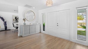 Ein modernes Interieur mit Holzboden, weißen Wänden, einem runden Spiegel, einer weißen Konsole und einer zur Außenseite führenden Tür.