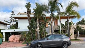 A modern building with a covered outdoor area, a parked car, and palm trees. - villa Bouznika Bay by Saloua (Cherrat)