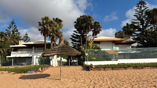 A beachfront property with a thatched umbrella, palm trees, and modern buildings. - villa Bouznika Bay by Saloua (Cherrat)