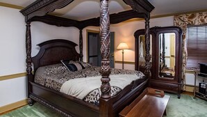 Una cama con dosel, cabecera y piecera de madera, una mesita de noche y un espejo.