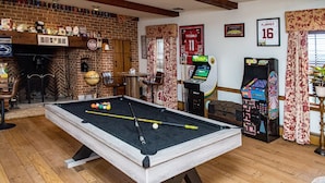 Una mesa de billar con bolas de billar, una chimenea y máquinas de videojuegos en una sala con suelo de madera y paredes de ladrillo.