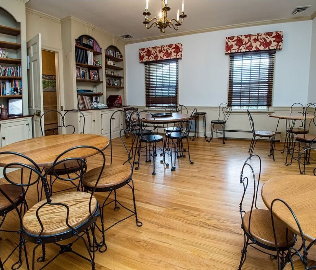 A dining area with round tables and chairs, wooden flooring, and a chandelier.