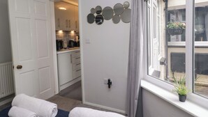 A room with a bed, a window with a view, a wall-mounted mirror, and a door leading to a kitchen.