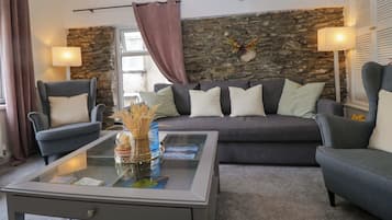 A living room with a stone wall, a gray sofa, two armchairs, a glass coffee table, and two floor lamps.
