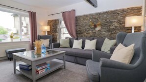 A living room with a grey sofa, a glass coffee table, and a stone wall. - Courtyard Cottage (Grange-over-Sands)
