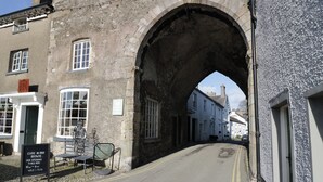 A street under an archway with buildings on either side, a signboard, and a bench. - Courtyard Cottage (Grange-over-Sands)