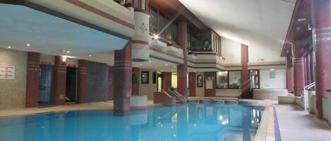 An indoor swimming pool with multiple levels of balconies, clear signage, and a tiled floor.