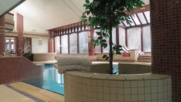 Una piscina interior con pared de azulejos, un banco y una planta en maceta.
