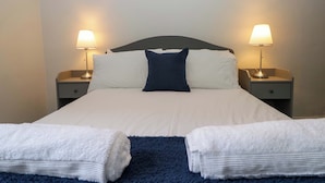 A neatly made bed with white and blue bedding, two bedside lamps, and two folded towels on the floor.