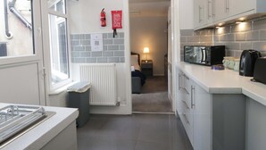 A modern kitchen with a built-in microwave, coffee maker, and kettle. There is a window with a view of the outside, a radiator, and a door leading to another room. - Courtyard Cottage (Grange-over-Sands)