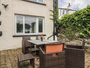 An outdoor patio with wicker furniture, a table, and a bottle of champagne. - Courtyard Cottage (Grange-over-Sands)