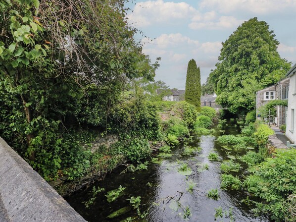 A narrow waterway flanked by dense greenery and stone walls, with buildings on one side. - Courtyard Cottage (Grange-over-Sands)