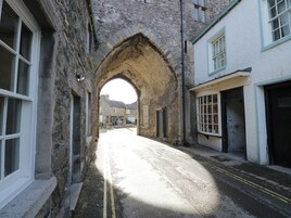 A narrow street with stone buildings, an archway, and a car parked in the distance.