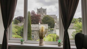 A window with curtains, a view of a castle, and two small potted plants on the windowsill. - Courtyard Cottage (Grange-over-Sands)