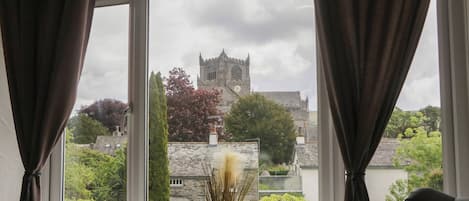 A window with curtains, a view of a castle, and two small potted plants on the windowsill.