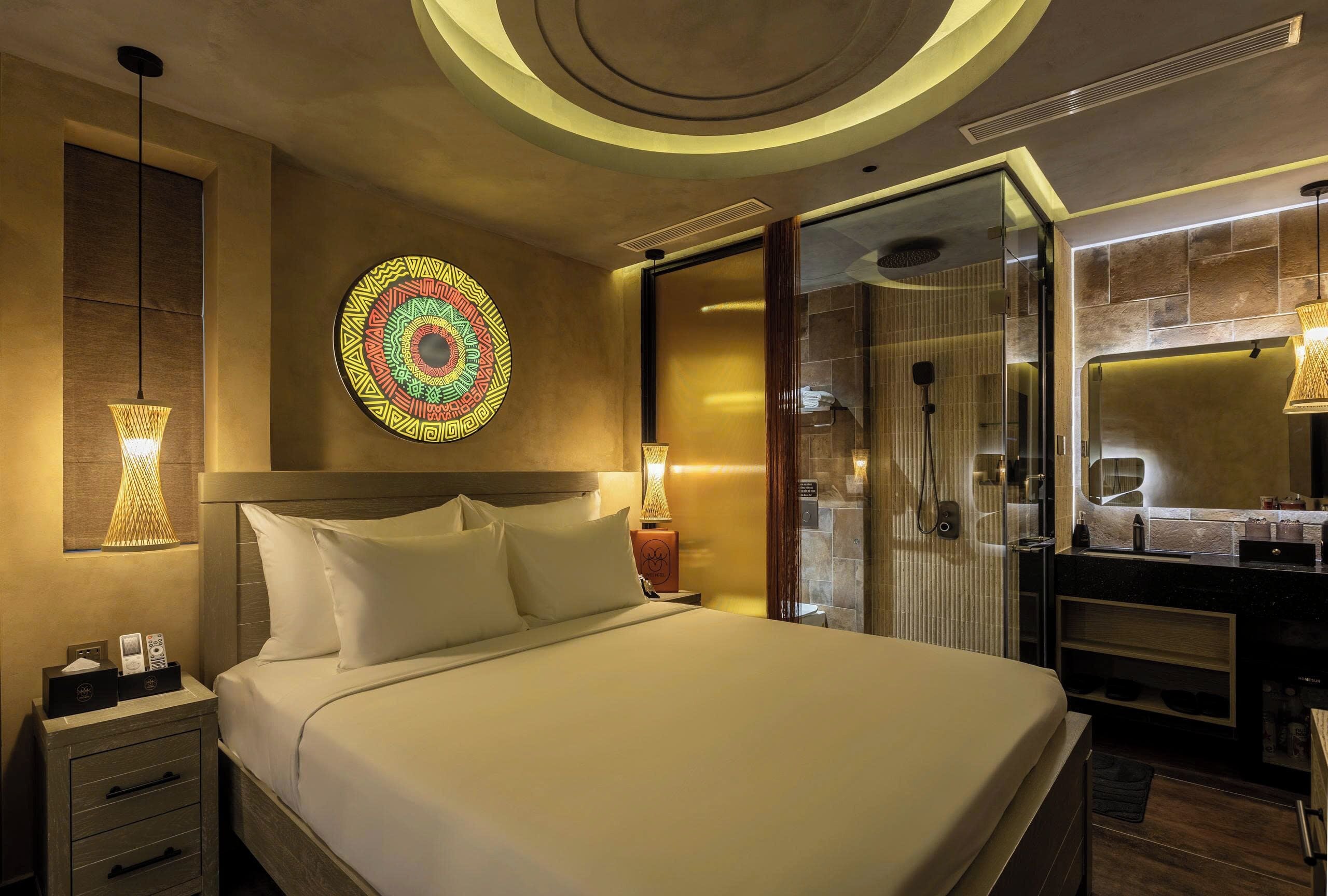 A modern hotel room with a large bed, a wall-mounted decorative plate, a glass shower enclosure, and a vanity with a mirror.
