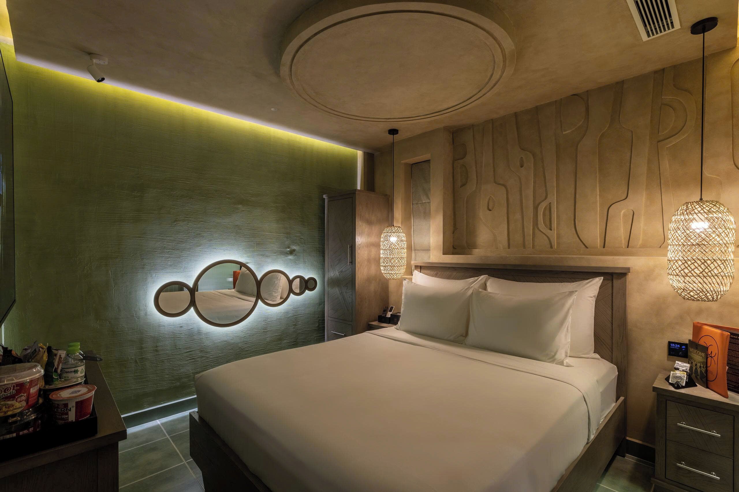 Una habitación de hotel moderna con una cama grande, una lámpara fijada a la pared y un cabecero de madera.