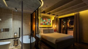 A hotel room with a bed, a round bathtub, a glass shower enclosure, a wall-mounted artwork, and a nightstand with a lamp. - PYNT HOTEL 8 (Ho Chi Minh City)