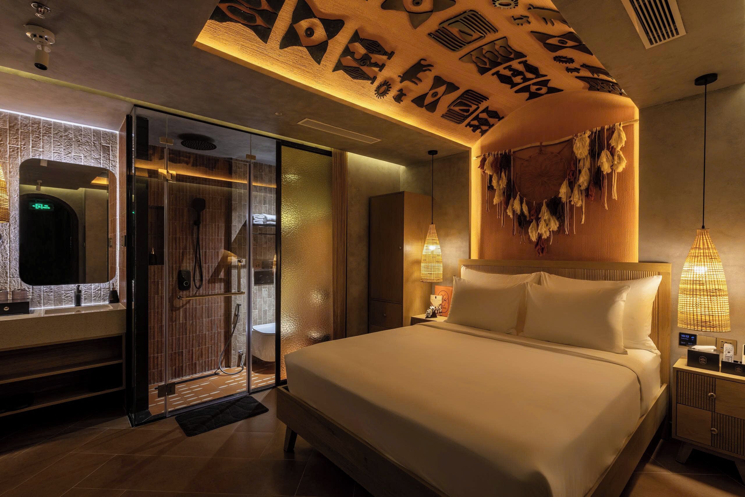 A modern hotel room with a large bed, a glass shower enclosure, and a unique ceiling design.