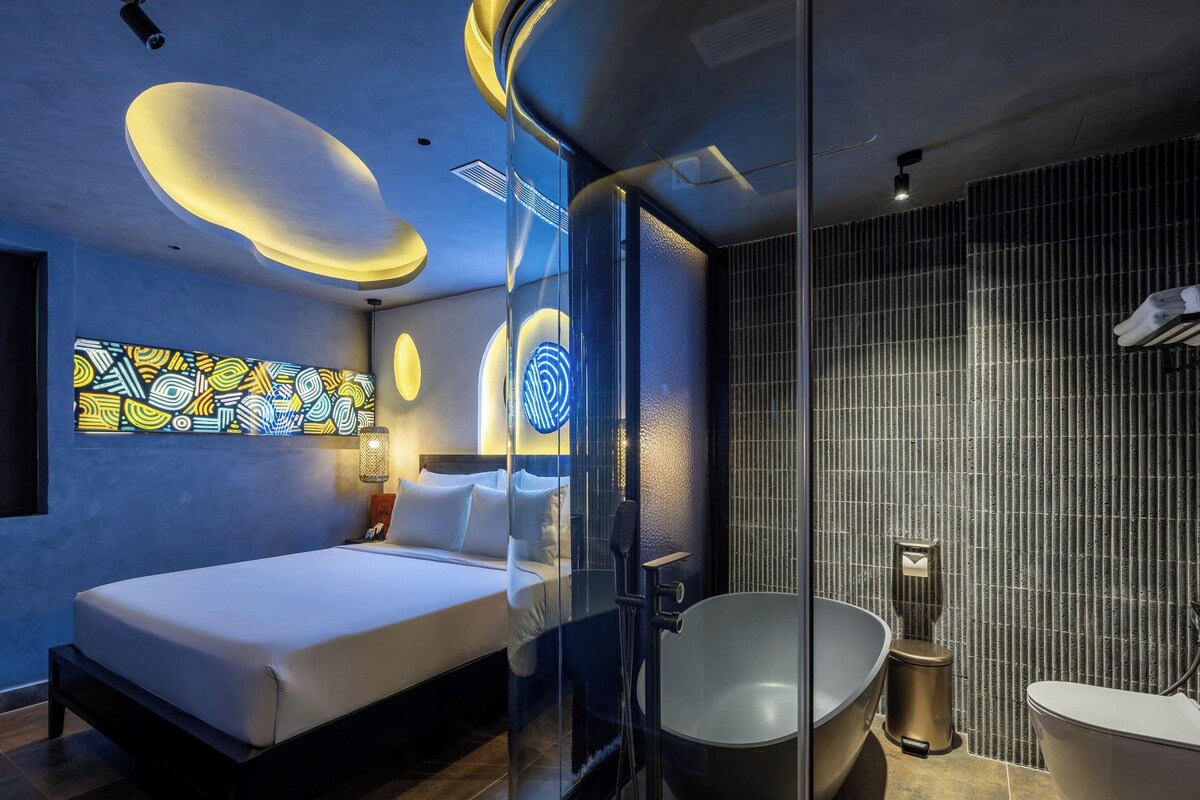 Habitación de hotel moderna con una cama grande, ducha con paredes de vidrio, bañera y una obra de arte colgada en la pared.