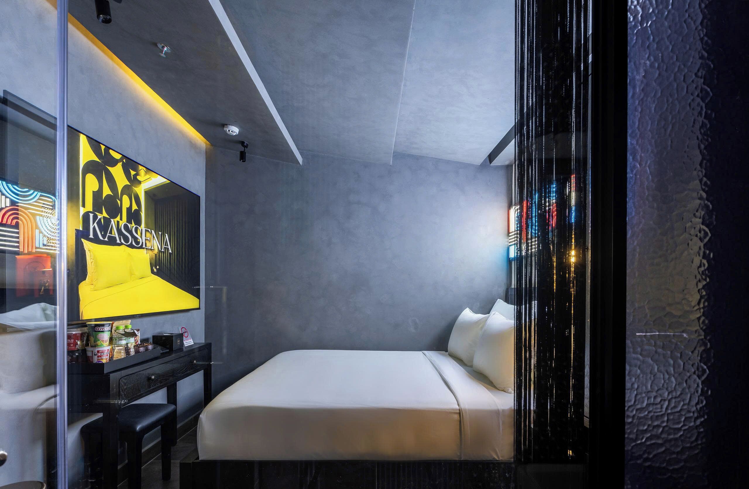 A modern hotel room with a bed, a TV, a small table, and a glass partition.
