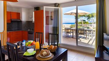 A dining area with a table set for breakfast, a kitchen with orange cabinets, and a balcony with outdoor seating.
