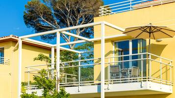 A yellow building with a balcony, glass railings, and a tree in the background.
