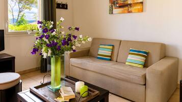A living room with a beige sofa, a glass vase with flowers, a candle, and a tray with books and a remote control.