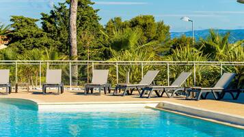 A swimming pool with lounge chairs and a metal railing, surrounded by greenery and trees.