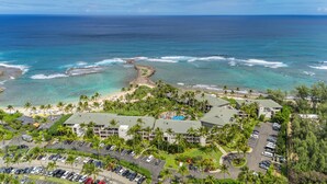 Ein Resort mit mehreren Gebäuden, einem Parkplatz und einem Strand mit klarem, blauem Wasser.