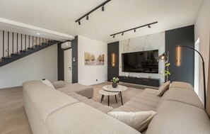 A modern living room with a large sofa, a small table with a vase, a flat-screen TV, and a staircase. - Villa Ikić Zadarvillas (Sukosan)